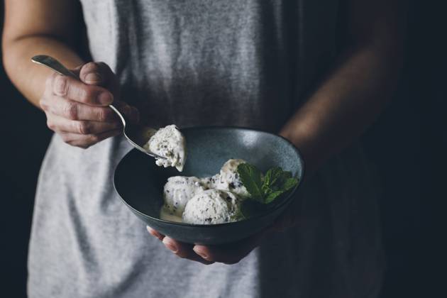 Crop view of anonymous woman with spoon in hand and holding bowl with stracciatella ice cream balls decorated with mint leaves Copyright: xVirginiaxMartinx Model Released