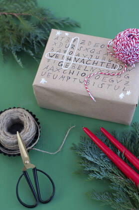IMAGO Creative: Weihnachten, DIY, Geschenke verpacken - Nachhaltigkeit Scissors, string and word search puzzle on wrapped Christmas present GISF00714
