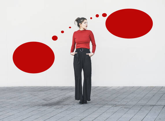 Young woman with hands in pockets standing against blank red speech bubble on wall model released Symbolfoto UUF22067