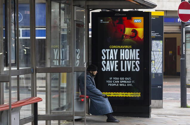 (210110) -- LONDON, Jan. 10, 2021 -- A person wearing a face mask sits next to an advertising board reading Stay Home Save Lives at a bus stop in London, Britain, Jan. 10, 2020. The coronavirus-related deaths in Britain surpassed 80,000 on Saturday with another 1,035 reported in the country. ) BRITAIN-LONDON-COVID-19-CASES HanxYan