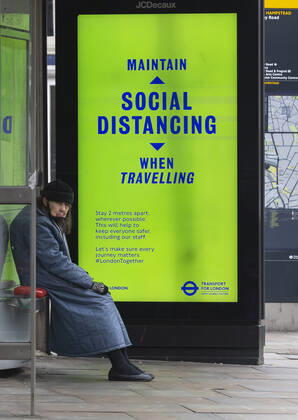 (210110) -- LONDON, Jan. 10, 2021 -- A person wearing a face mask sits next to an advertising board reading Maintain social distancing when travelling at a bus stop in London, Britain, Jan. 10, 2021. The coronavirus-related deaths in Britain surpassed 80,000 on Saturday with another 1,035 reported in the country. ) BRITAIN-LONDON-COVID-19-CASES HanxYan