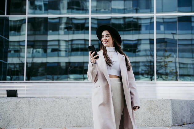 Smiling woman with smart phone looking away while standing against building model released Symbolfoto EBBF01484