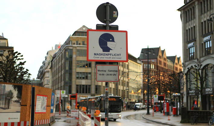 Ein an einem Laternenpfahl befestigtes Schild weist darauf hin, dass in der Mönckebergstraße in Hamburg zu bestimmten Zeiten Maskenpflicht herrscht. Altstadt Hamburg