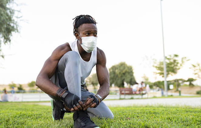 IMAGO Creative: Kulturelle Folgen der Pandemie: Gesundheitsbewußtsein und Alleinsein Athlete wearing face mask tying lace of shoe while crouching on ground model released Symbolfoto JCCMF00165