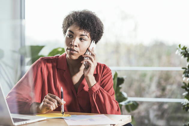 Woman talking on mobile phone and looking at laptop at desk model released Symbolfoto property released UUF22462