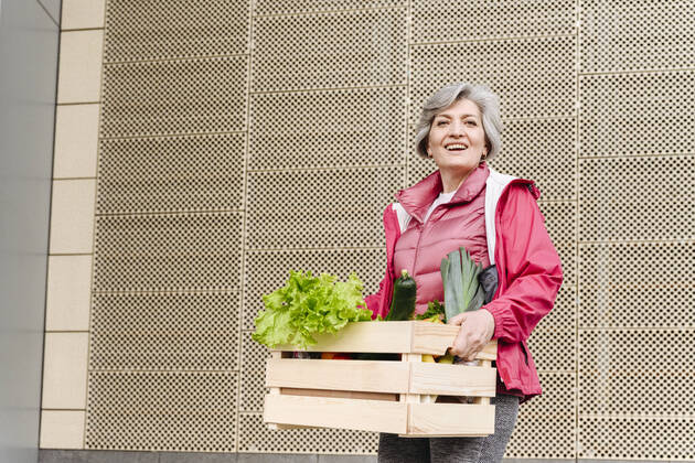 Happy mature woman with food crate against iron pattern wall model released Symbolfoto VYF00371