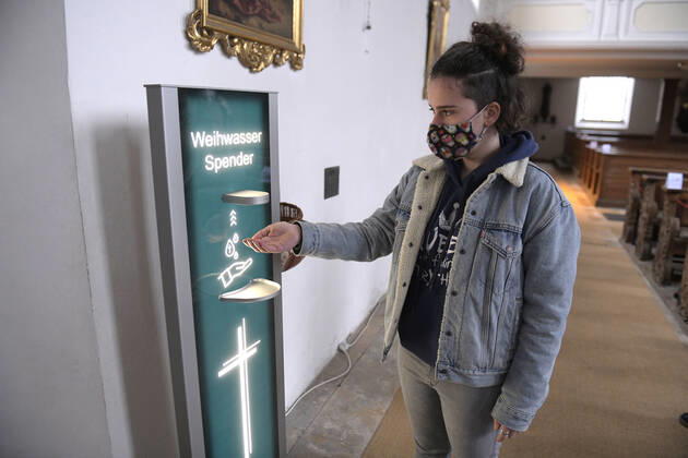30.01.2021, Kirchen in Bayern, Corona-Regeln in einer Kirche in Bayern, Eine junge Kirchenbesucherin mit Mundschutz lässt sich Weihwasser vom Automatischen Spender auf die Hand geben. (Modelreleased) Der von der Mindelheimer Firma Elektro-Bauer neuentwickelte, Corona-Konforme Weihwasser-Spender mit berührungslosem Ultraschall-Bewegungs-Sensor sichert die Einhaltung der Hygienemassnahmen für die Gläubigen. 30.01.2021, Kirche in Corona-Zeiten 30.01.2021, Kirche in Corona-Zeiten