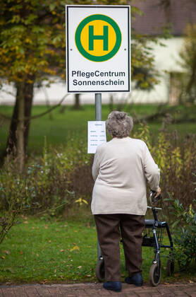 Schein - Bushaltestelle fuer Demenzkranke Eine Seniorin betrachtet am 29.10.2014 im Garten des Pflegecentrums Sonnenschein in Gerstungen ( Thueringen ) den Fahrplan an einem Bushaltestellenschild . Hier faehrt kein Bus - die Atrappe hilft, demenzkranke Bewohner vor einem Umherirren zu schuetzen. Gerstungen Thüringen DEUTSCHLAND