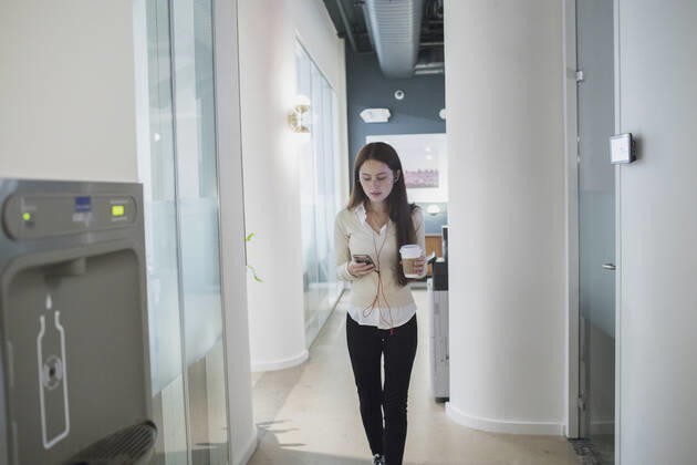 Young woman having a conversation on her smart phone holding a coffee cup in an office. model release HEX17003_TP_9410 Copyright: xTOBIASxPRASSEx