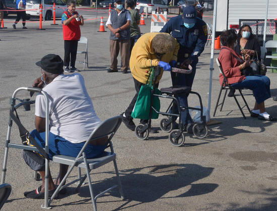 A firefighter helps a senior citizen as she arrives to receive a COVID-19 vaccination shot at the South Park Recreation Center in Los Angeles on Thursday, February 11, 2021. To boost vaccination among people of color, L.A. county plans more sites, better messaging and access to transit. Black, Latino and Native American seniors are being vaccinated at lower rates than other groups.  LAP2021021101 JIMxRUYMEN