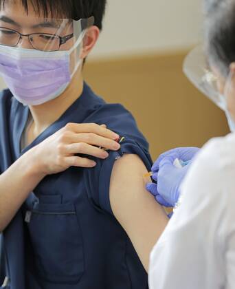 Japan begins COVID-19 vaccine to health workers A health worker inoculates a colleague with COVID-19 vaccine at the Tokyo Medical Center in Tokyo s Meguro Ward on Feb. 17, 2021. Japan began COVID-19 vaccinations the same day, with the first shots given at the state-run hospital. (Pool photo) 