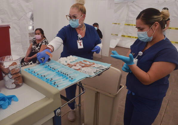 A physician assistant picks up a syringe prepared with the COVID-19 Moderna vaccine from a tray for a local resident waiting to be inoculated at the Kedren Community Health Center in South Los Angeles on Tuesday, February 16, 2021. To boost vaccination among people of color, L.A. county plans more sites, better messaging and access to transit. Black, Latino and Native American seniors are being vaccinated at lower rates than other groups.  LAP2021021605 JIMxRUYMEN