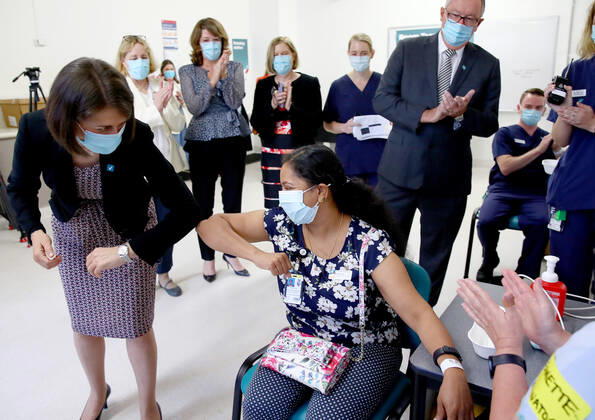 NSW COVID19 VACCINE ROLLOUT, Gayathry Vellangalloor Srinivasan, an Environmental Services Supervisor, is watched by NSW Premier Gladys Berejiklian (left), NSW Chief Medical Health Officer Kerry Chant (fourth right) and NSW Health Minister Brad Hazzard (second right) as she receives the states first Pfizer vaccination at the Royal Prince Alfred Hospital Vaccination Hub in Sydney, Monday, February 22, 2021. Australia will begin its roll out of the Pfizer coronavirus vaccine on Monday, the country s most complicated logistical exercise to date. ( NO ARCHIVING, EDITORIAL USE ONLY, NO USE IN BOOKS WITHOUT CONSENT SYDNEY NSW AUSTRALIA Copyright: xTobyxZernax 20210222001522236514