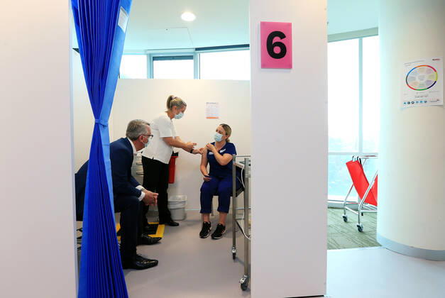 VIC COVID19 VACCINE ROLLOUT, Covid screening nurse Grace Gibney (right) receives one of the first Pfizer coronavirus vaccines from Nurse practitioner Sonja Elia as Health Minister Martin Foley (left) watches on at Austin Health in Melbourne, Monday, February 22, 2021. Australia will begin its roll out of the Pfizer coronavirus vaccine on Monday, the country s most complicated logistical exercise to date. ( NO ARCHIVING, EDITORIAL USE ONLY, NO USE IN BOOKS WITHOUT CONSENT MELBOURNE VIC AUSTRALIA Copyright: xMARKxSTEWARTx 20210222001522293431