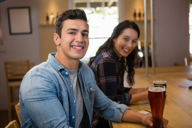 Portrait of smiling friends enjoying drinks at restaurant Portrait of smiling young friends enjoying drinks at counter in restaurant, model released, Cape Town, South Africa, 28.03.2017, 1024184.jpg, friendship, togetherness, bonding, holding, beer, drink, food and drink, refreshment, lifestyle, leisure, casual clothing, smiling, enjoying, alcohol, bar counter, bar, relaxing, pretty, attractive, beautiful, handsome, restaurant, sitting, food and drink establishment, counter, wood, happiness, drinking glass, beer glass, chair Indoors,Portrait,Looking at camera,Day,Half length