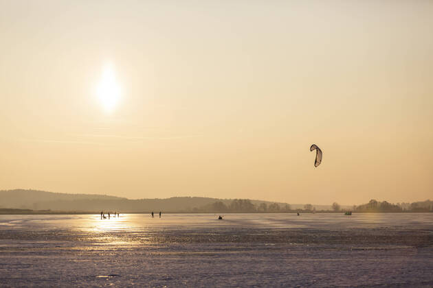 IMAGO Creative: Alternativer Wintersport Germany, Brandenburg, Rangsdorf, Winter landscape with frozen lake, people playing with kite ASCF01536