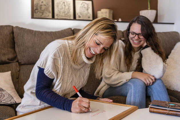 Smiling female psychologist writing on whiteboard while sitting with young woman in office model released Symbolfoto property released DLTSF01581