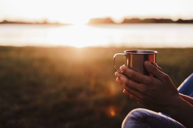 Hands of mid adult woman holding drink against lake during sunset model released Symbolfoto EBBF02205