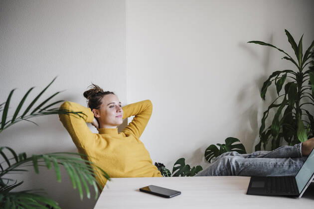 Smiling woman with hands behind head relaxing while sitting by table at home model released Symbolfoto property released EBBF02409