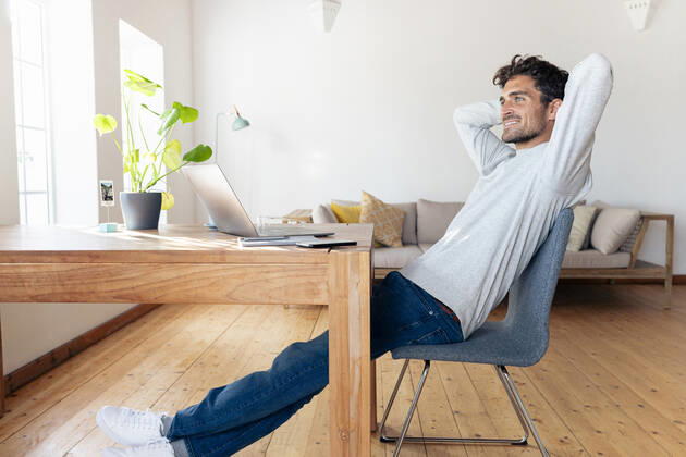 Smiling man with hands behind head relaxing while sitting on chair at home model released Symbolfoto property released SBOF02408