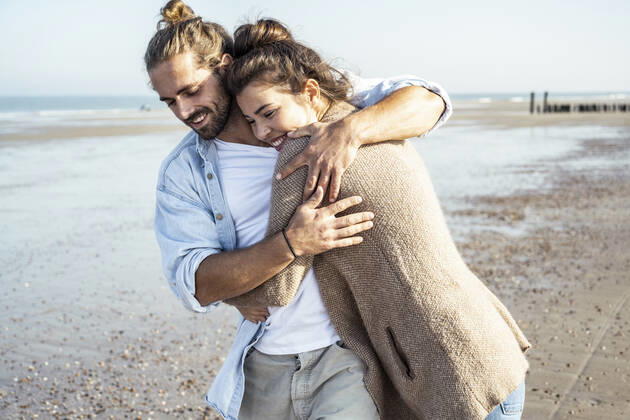 Smiling girlfriend embracing boyfriend at beach on sunny day model released Symbolfoto UUF22742