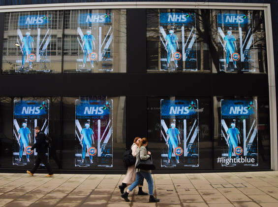 February 25, 2021, London, United Kingdom: People walk past screens displaying NHS National Hero at the Flannels store on Oxford Street in London..The screens at the store are currently showing a series of artworks as part of the LightItBlue campaign in support of the NHS. London United Kingdom - ZUMAs197 20210225_zaa_s197_087 Copyright: xVukxValcicx