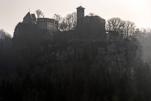 04.03.2021, Deutschland,Sachsen, Sächsische Schweiz, Hohnstein: Blick auf die Burg Hohnstein im Schein der aufgehenden Sonne. Die einzige bis heute erhaltene rechtselbische Burg in der Sächsischen Schweiz wurde vermutlich im 12. Jahrhundert als böhmische Grenzfeste zur Markgrafschaft Meißen gebaut. Heute befinden sich hier unter anderem ein Museum und eine Gedenkstätte. Die Burg liegt malerisch unmittelbar am Nationalpark Sächsische Schweiz auf einem Felssporn über dem Polenztal. Tausende Touristen besuchen Burg und Stadt in der Feriensaison.
