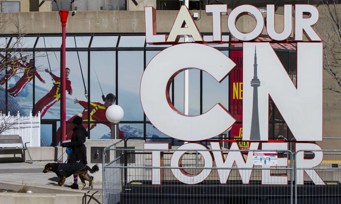 (210305) -- TORONTO, March 5, 2021 -- A woman wearing a face mask walks a dog past the CN Tower sign in Toronto, Canada, on March 5, 2021. The global COVID-19 pandemic, including the associated restrictions and lockdowns over the past 12 months, have resulted in 8.35 billion Canadian dollars (about 6.6 billion U.S. dollars) in lost economic activity from visitor spending in Toronto, according to a press release by Destination Toronto on Thursday. (Photo by Xinhua) CANADA-TORONTO-COVID-19-TOURISM ZouxZheng 