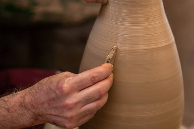 Crop unrecognizable sculptor with equipment giving shape while sculpting with brown clay on throwing wheel, Model released Copyright: xMiguelxVallsx MR