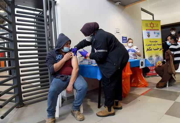 A medic from Israel s Magen David Adam emergency agency inoculates a Palestinian worker with the first dose of the Moderna COVID-19 vaccine at the Lamed Hei Checkpoint between Gush Etzion and Beit Shemesh, on Monday, March 8, 2021. Israel started a two week campaign to vaccine some 100,000 Palestinian workers from the West Bank who hold permits to work in Israel and Jewish settlements. The vaccination campaign is a joint project by the Israeli Heath Ministry, Ministry of Defense, Land Crossing Authority and the Coordination of Government Activities in the Territories.  JER2021030807 DEBBIExHILL