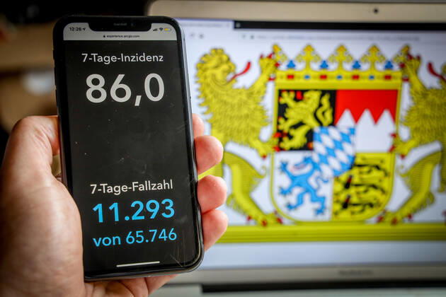 Coronavirus in Deutschland - Covid-19-Dashboard des Robert Koch-Institut DEU, Deutschland, Bayern, 14.03.2021: Die 7-Tage-Inzidenz für das Bundesland (Fälle letzte 7 Tage 100.000 EW) wird auf einem iPhone angezeigt, im Hintergrund das Landeswappen
