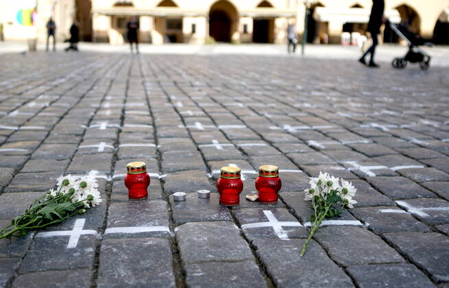 (210323) -- PRAGUE, March 23, 2021 -- Flowers and candles are seen on the ground of the Old Town Square where thousands of white crosses are painted in memory of the victims of the COVID-19 pandemic in Prague, Czech Republic, on March 22, 2021. (Photo by Xinhua) CZECH REPUBLIC-PRAGUE-COVID-19-VICTIMS-MEMORIAL DanaxKesnerova 