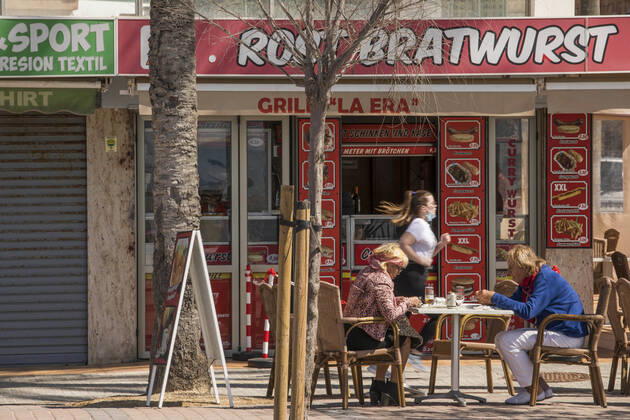 March 22, 2021, Mallorca, Spain: A couple sitting in the sausage restaurant Rostbratwurst with a woman running in the background at Playa de Palma in Mallorca. Spain - ZUMAm210 20210322_ztp_m210_001 Copyright: xJohn-PatrickxMorarescux