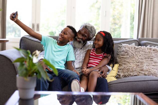 Senior African American man and his grandchildren at home Senior African American man and his grandchildren enjoying their time at home together, sitting on a couch, embracing, smiling, using a smartphone, taking a selfie, model released, , property released, Cape Town, South Africa, 19.02.2020, 1340053.jpg, people,family,grandfather,granddad,granddaughter,grandson,siblings,brother,sister,childhood,together,closeness,interacting,sitting,couch,holding,using,phone,mobile phone,smartphone,connection,communication,taking,photo,photograph,selfie,real people,home,house,domestic life,lifestyle,enjoying,free time,leisure,relaxing,weekend,summer,sunny,love Child,Girl,Female,Mixed-Race,Mid Adult,Man,Male,Black Indoors,Front view,Day,Three Quarter Le