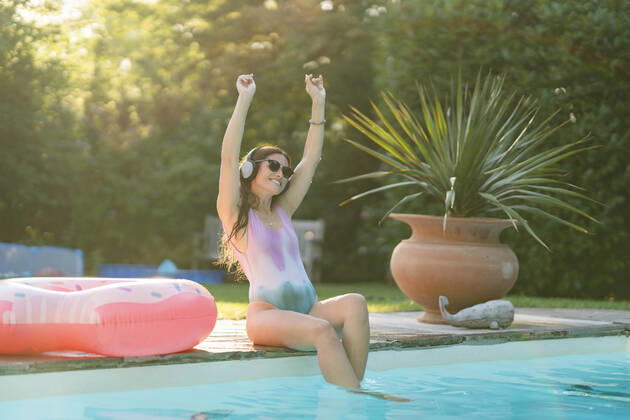 Cheerful woman in swimwear enjoying music while sitting at pool model released Symbolfoto property released AKLF00065