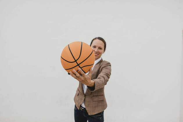Playful female professional with basketball standing against white wall while taking break model released Symbolfoto DMGF00517