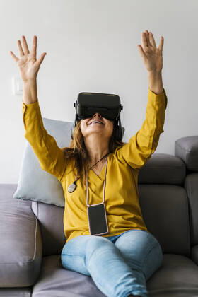Mature woman gesturing while wearing Virtual reality headset sitting on sofa at home model released Symbolfoto property released EGAF02066