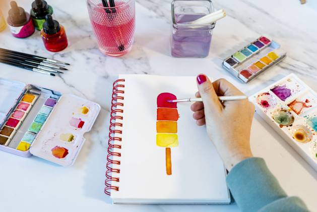 Woman painting popsickle ice cream with watercolor in book on table model released Symbolfoto property released GEMF04682