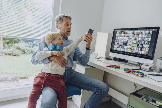 Son distracting father through smart phone while video conferencing at home office model released Symbolfoto property released MFF07200