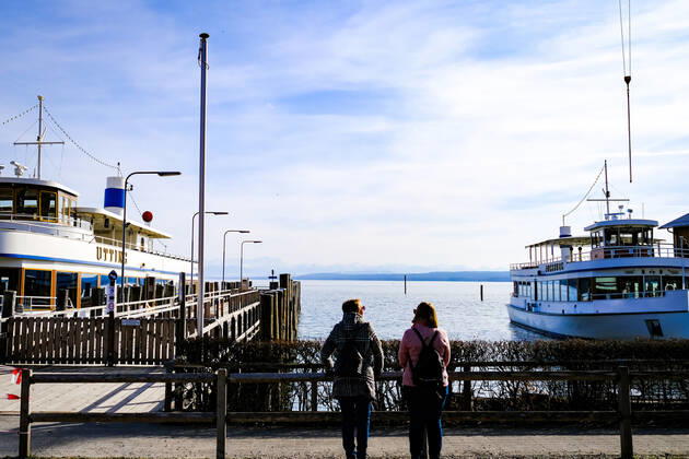 Frühlingswetter am Ammersee 25.03.2021: Ausflügler vor Schiffen bei Frühlingswetter im Hafen von Stegen (Inning am Ammersee; Oberbayern) mit Blick in Richtung Alpen. Inning Bayern Deutschland