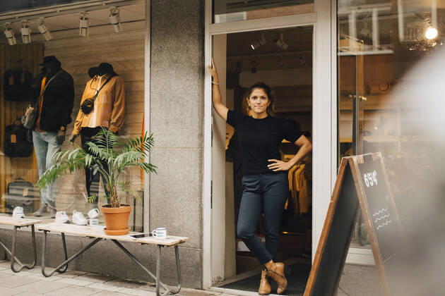 Female entrepreneur with hand on hip standing on doorway of retail store Sweden, Stockholm, model released, property released Copyright: xMaskotx , MA85327