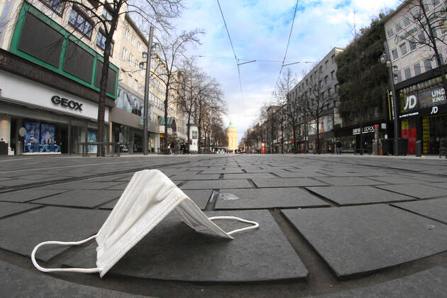 Getragene Mund-Nase-Bedeckungsmaske liegt auf dem Pflaster der menschenleeren Fußgängerzone und Einkaufsstraße Planken in der Innenstadt von Mannheim, Baden Württemberg, Deutschland