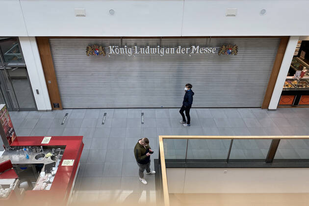 Themenbild: Coronavirus Pandemie Folgen fuer die Gastronomie. Geschlossenes bayerisches Restaurant im Einkaufszentrum Riem Arkaden in Muenchen Riem.Ein Metallrollo ist heruntergelassen-davor gehen Passanten mit Mundschutz,Maske. Schliessung-Folge der Corona Pandemie,Lockdown,Shutdown,Inzidenzwert.