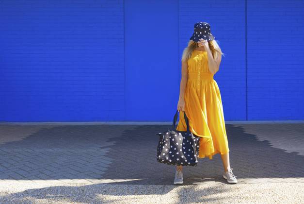 Mature woman with duffel bag and bucket hat in front of blue wall model released Symbolfoto AZF00274