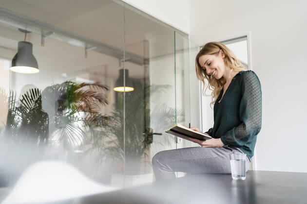 IMAGO Creative: Kreative Renaissance -- der junge Entrepreneur Smiling female entrepreneur reading diary while sitting on conference table in office model released Symbolfoto property released DIGF15009