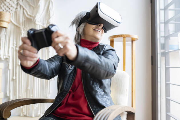 Smiling woman with game controller playing through virtual reality simulator at home model released Symbolfoto property released JCCMF01911