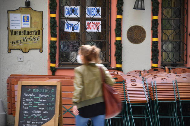 Themenbild: Coronavirus Pandemie Folgen fuer die Gastronomie: GASTRO WIEDER OEFFNEN SOFORT Im Fenster eines bayerischen Restaurants in Muenchen fordern die Eigentuemer die sofortige Oeffnung der Gastronomie. Uebereinander gestapelte Stuehle und Tische lehnen an der Hauswand. Passanten gehen mit Mundschutz,Maske vorbei.