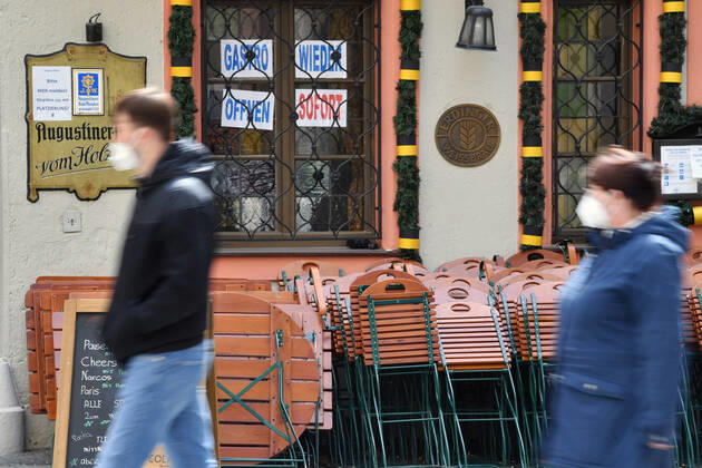Themenbild: Coronavirus Pandemie Folgen fuer die Gastronomie: GASTRO WIEDER OEFFNEN SOFORT Im Fenster eines bayerischen Restaurants in Muenchen fordern die Eigentuemer die sofortige Oeffnung der Gastronomie. Uebereinander gestapelte Stuehle und Tische lehnen an der Hauswand. Passanten gehen mit Mundschutz,Maske vorbei.