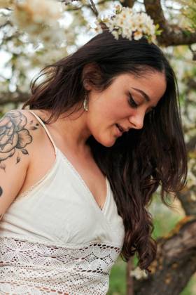 Young female with tattooed arm wearing white dress and standing in flowers of tree looking down, Model released, Property released Copyright: xCristianxBlazquezx MR