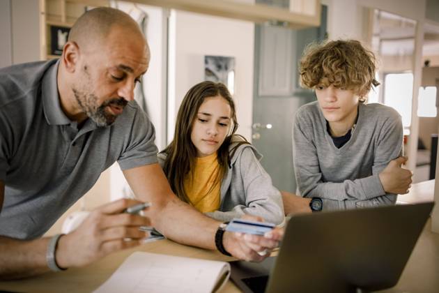 Brother and sister looking at father explaining finance with credit card at kitchen island Sweden, Stockholm, model released, property released Copyright: xMaskotx , MA86519